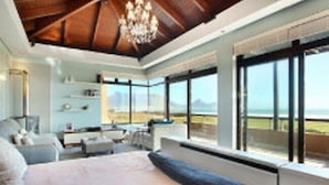 A spacious bedroom with a large bed, a chandelier, and a view of the ocean. - Luxury Vacation Villa (Cape Town)