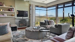 A modern living room with a fireplace, comfortable seating, and a large window offering a view of the outdoors. - Luxury Vacation Villa (Cape Town)