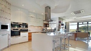 A modern kitchen with a central island, bar stools, and a large window offering a view of the outdoors. - Luxury Vacation Villa (Cape Town)