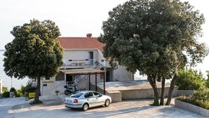 A building with a red-tiled roof, a covered outdoor area, and a parked car. - Guest House Fontana - Two Bedroom Apartment with Balcony and Sea View (Mlini)