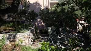 Un muro de piedra, dos sillones a rayas y un edificio con balcón.