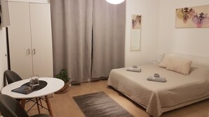 Ein Schlafzimmer mit Bett, Schreibtisch mit Stuhl, Kleiderschrank, Topfpflanze und einem Bild an der Wand.