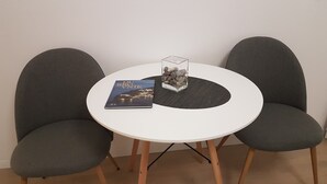 Ein runder, weißer Tisch mit zwei grau gepolsterten Stühlen. Auf dem Tisch liegt ein Buch mit dem Titel 'Du Vinik' und eine transparente Glasvase mit Steinen.
