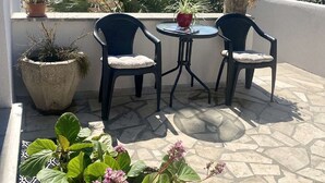 Eine Terrasse mit zwei Stühlen und einem Tisch, umgeben von Topfpflanzen und einem Steinboden.