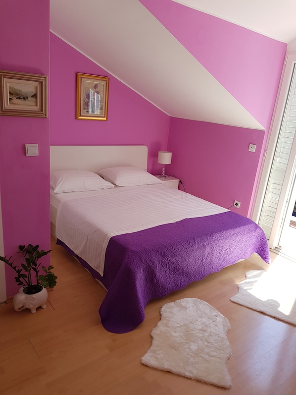A bedroom with a bed, a nightstand, a lamp, a potted plant, and a white rug.