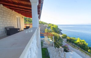 Un balcón con muro de piedra, mobiliario exterior y vista al mar.