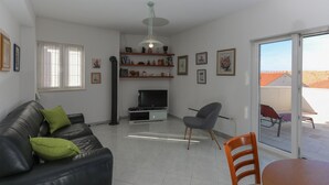 A living room with a black leather sofa, a grey armchair, a TV on a stand, and a glass door leading to an outdoor area. - Apartment Perina - Two Bedroom Apartment with Terrace and Sea View (Sutivan)