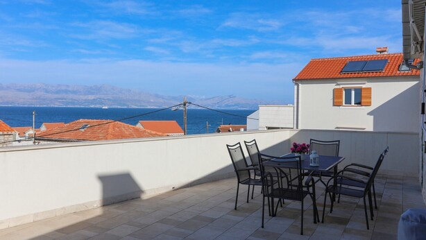 A terrace with a table and chairs, overlooking a coastal area with buildings and a clear sky. - Apartment Perina - Two Bedroom Apartment with Terrace and Sea View (Sutivan)