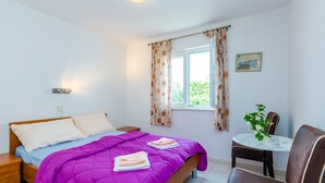 A bedroom with a bed, a bedside table, a chair, a small table with a vase, and a window with curtains. - Villa Bind Basic Double Room,Patio & Garden ViewR3 (Obod)