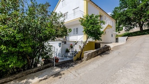 A two-story building with a white facade and yellow trim, a staircase leading to the upper floor, and a small garden area with potted plants. - Villa Bind Basic Double Room,Patio & Garden ViewR3 (Obod)