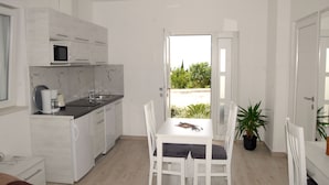 Una cocina moderna con armarios blancos, microondas y cafetera. Hay una mesa de comedor con sillas y una planta en maceta.