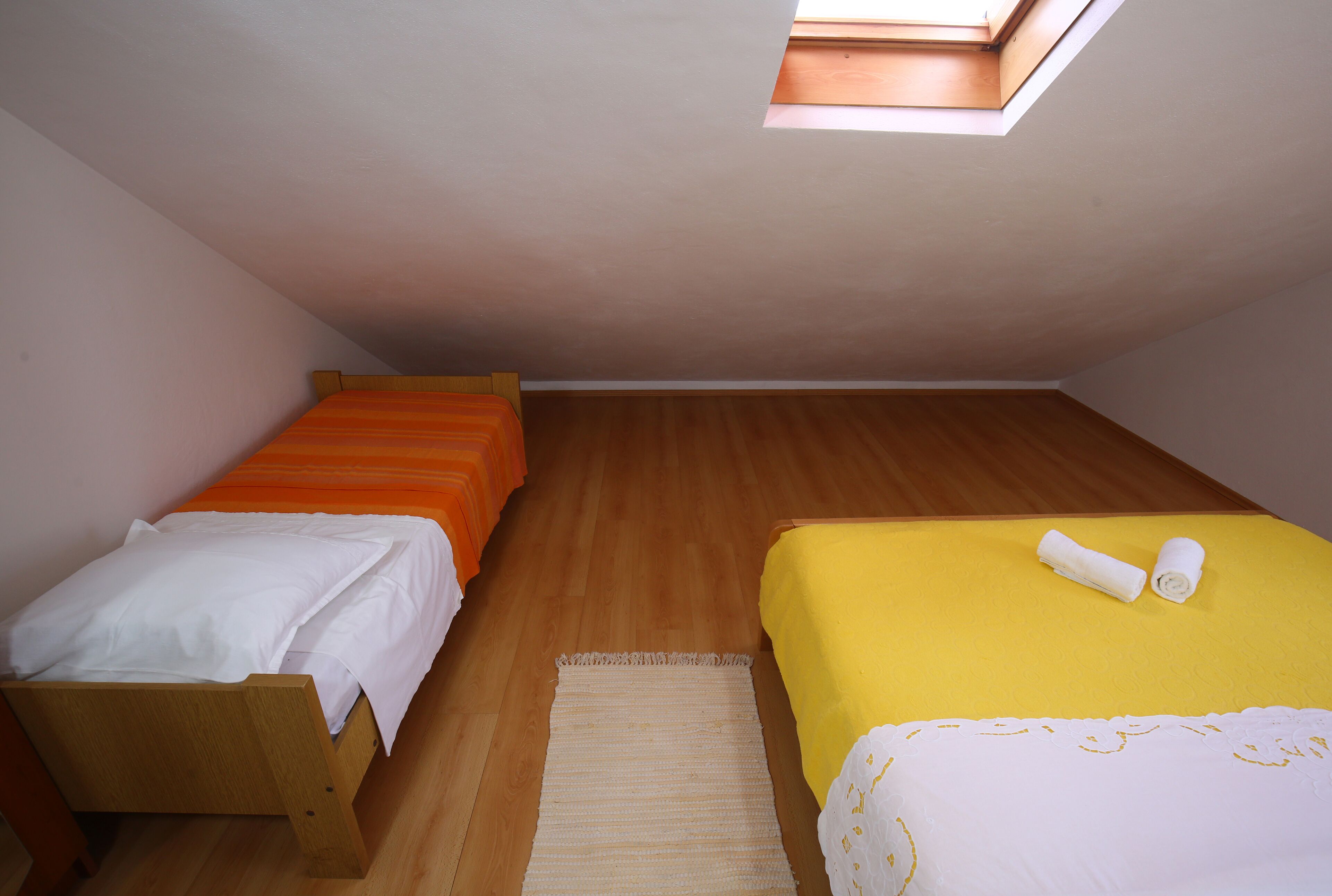 Een kleine kamer met twee bedden, dakraam en houten vloer.