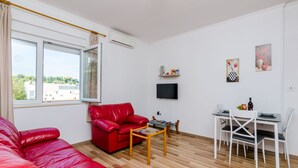 Un salon moderne avec un canapé en cuir rouge, une table à manger avec des chaises, un téléviseur à écran plat fixé au mur et des œuvres d’art accrochées aux murs.