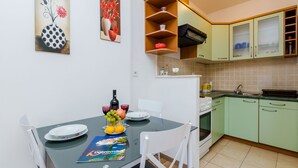 Un coin repas avec une table dressée pour deux personnes, une cuisine avec des meubles verts et un tableau accroché au mur.