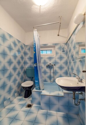 A bathroom with blue patterned tiles, a white toilet, a shower with a blue curtain, and a sink with a mirror. - Apartments Nena (ST) - Two Bedroom Apartment with Terrace and Sea View (Pisak)