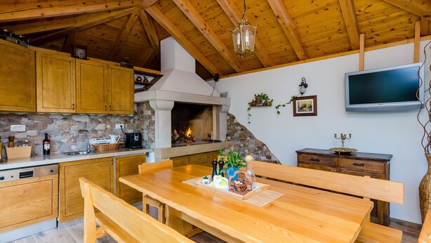 Eine rustikale Küche mit Holzschnitzschränken, einer Steinwand, einem Kamin und einem Essbereich mit Bänken.