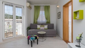 Ein modernes Wohnzimmer mit einem grauen Sofa, einem kleinen runden Tisch und einem farbenfrohen Hocker.