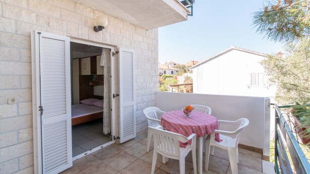 Un balcon avec une table et des chaises, un lit avec des volets et une vue sur les bâtiments voisins.