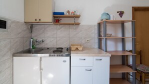 Une cuisine compacte équipée d’un évier, d’une cuisinière et de placards. Des étagères au-dessus du plan de travail servent à ranger divers ustensiles de cuisine.