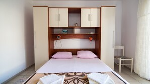 Une chambre à coucher avec un lit, deux oreillers roses, une armoire en bois, une chaise et une petite table sur laquelle est posé un cadre photo.