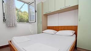 A neatly made bed with white linens, a wooden headboard, and light green cabinets above. - Apartments Neven - One Bedroom Apartment with Terrace and Garden View (A2) (Drace)