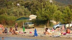 A beach with people sunbathing and swimming, a car parked nearby, and a building in the background. - Apartments Neven - One Bedroom Apartment with Terrace and Garden View (A2) (Drace)