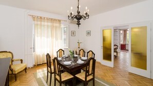 Een eetkamer met een houten tafel voor vier personen, een kroonluchter en een groot raam met gordijnen.