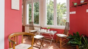 Een kamer met een rode muur, een raam met witte lijst, een tafel met stoelen en een radiator.