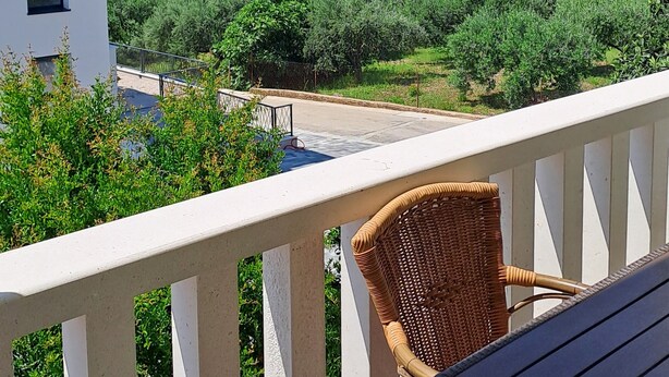 Un balcon avec une chaise en osier et une table, donnant sur un village côtier avec ses maisons et son église.