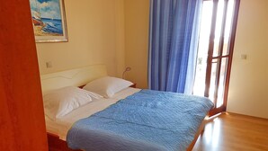 Une chambre à coucher avec un lit, des oreillers blancs, une couverture bleue, un tableau au mur et une fenêtre avec des rideaux.