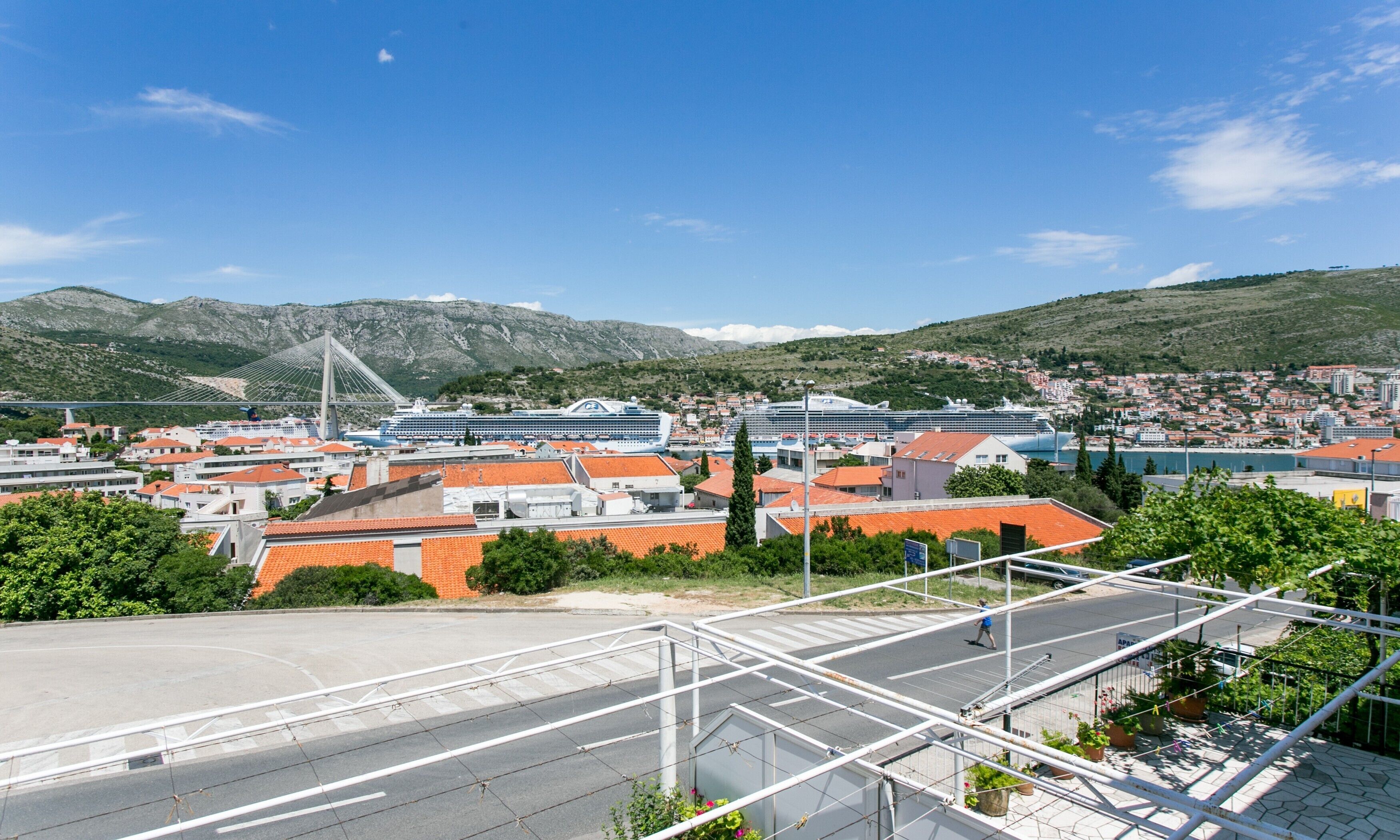 A coastal cityscape with a prominent bridge, cruise ships docked, and a mix of residential and commercial buildings.