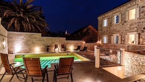 Un bâtiment en pierre doté d’une piscine, d’un espace extérieur aménagé et d’un palmier.