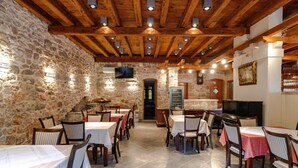 Un restaurant aux murs de pierre, aux poutres apparentes et aux tables dressées pour le repas.