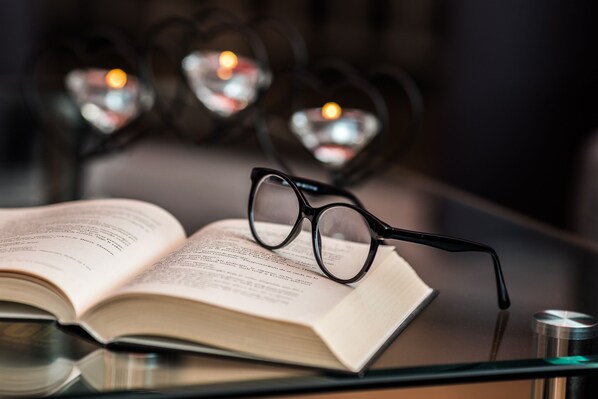 An open book with glasses on top, placed on a glass table.