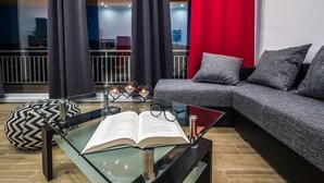 Ein modernes Wohnzimmer mit einem Glastisch, einer Couch und einem gemusterten Hocker.
