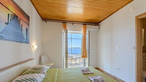 A hotel room with a bed, a chair, a window with a view, and a painting on the wall. - Rooms Sani- Double Room with Terrace and Sea View (S2) (Brela)