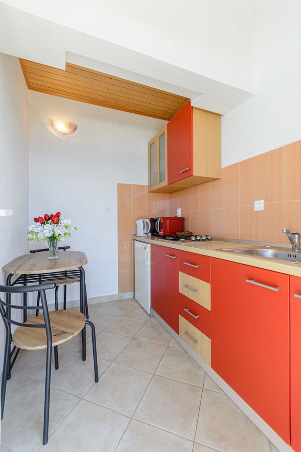 Une cuisine compacte avec des meubles de couleur rouge, un plafond en bois, une petite table à manger avec des chaises et un vase rempli de fleurs.