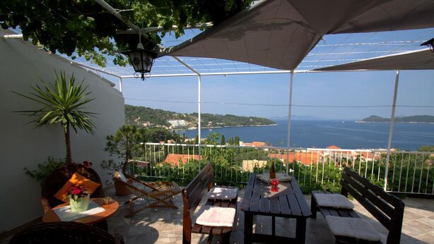 Un patio al aire libre con una mesa y bancos, una planta en maceta y vista al mar.