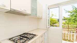 Une cuisine avec des meubles blancs, une cuisinière à gaz et une fenêtre donnant sur un jardin.