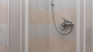 A corner shower with a handheld showerhead and a wall-mounted faucet.