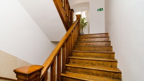 Una escalera de madera con barandilla, una planta en maceta en la parte superior y un letrero de salida verde en la pared.