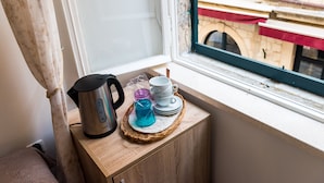 Una encimera de cocina con un hervidor, tazas y un frasco azul de vidrio sobre un tapete tejido.