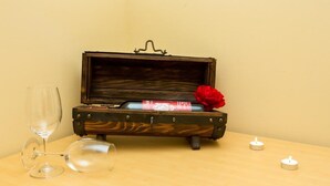 A wooden chest with a red rose and a wine bottle inside, accompanied by two wine glasses and two candles on a table. - Villa Iveta - Twin Room (Ground Floor) - Martina (Dubrovnik)