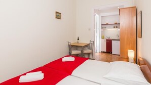 A small, clean room with a bed, a table with chairs, and a kitchenette in the background. - Villa Iveta - Twin Room (Ground Floor) - Martina (Dubrovnik)