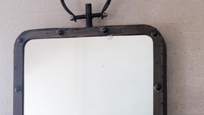 A rectangular mirror with a black frame and a ring at the top, mounted on a wall.