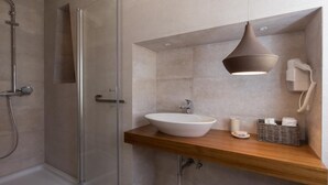 A modern bathroom with a glass shower enclosure, a wooden vanity with a white sink, and a pendant light.