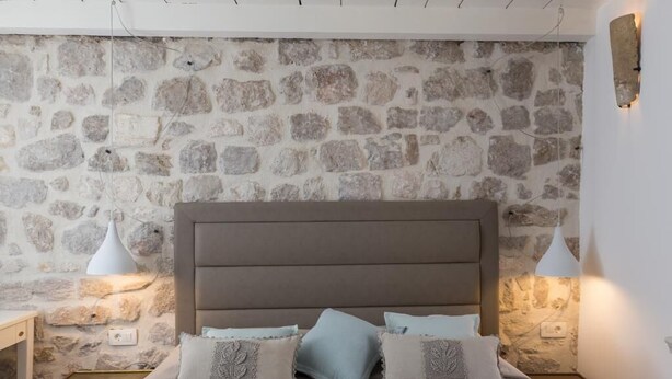 A bedroom with a stone wall, a bed with a headboard, two bedside tables, and two wall-mounted lamps.