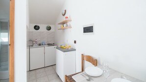 Eine kompakte Küche mit weißen Schränken, einem kleinen Kühlschrank und einem Essbereich mit einem Holztisch und einem Stuhl für zwei Personen.