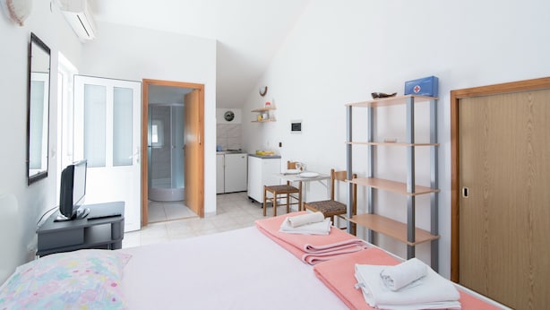 Ein Schlafzimmer mit Bett, Schreibtisch, Stuhl, einer kleinen Küchenzeile und einem durchgehenden Türspalt sichtbaren Badezimmer.
