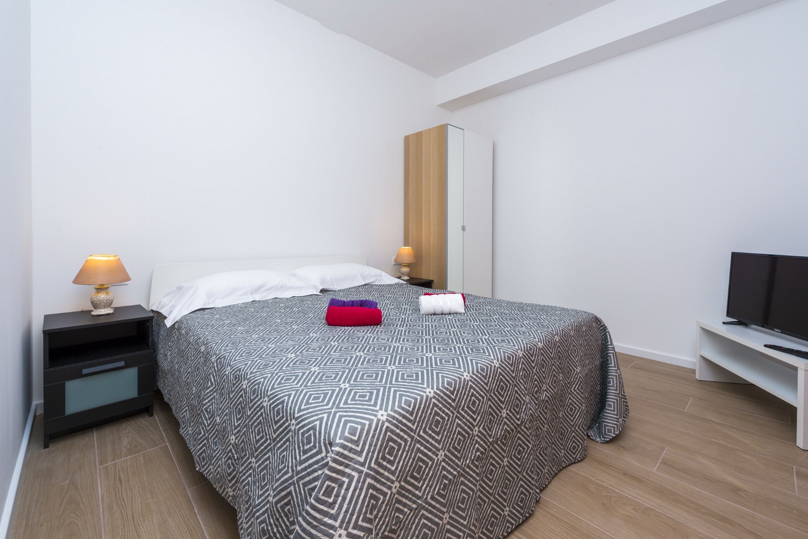 Un dormitorio con una cama, una mesita de noche, un televisor y un espejo.